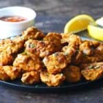 Golden colored chicken pieces garnished with cilantro. Lemon slices and sauce in background.