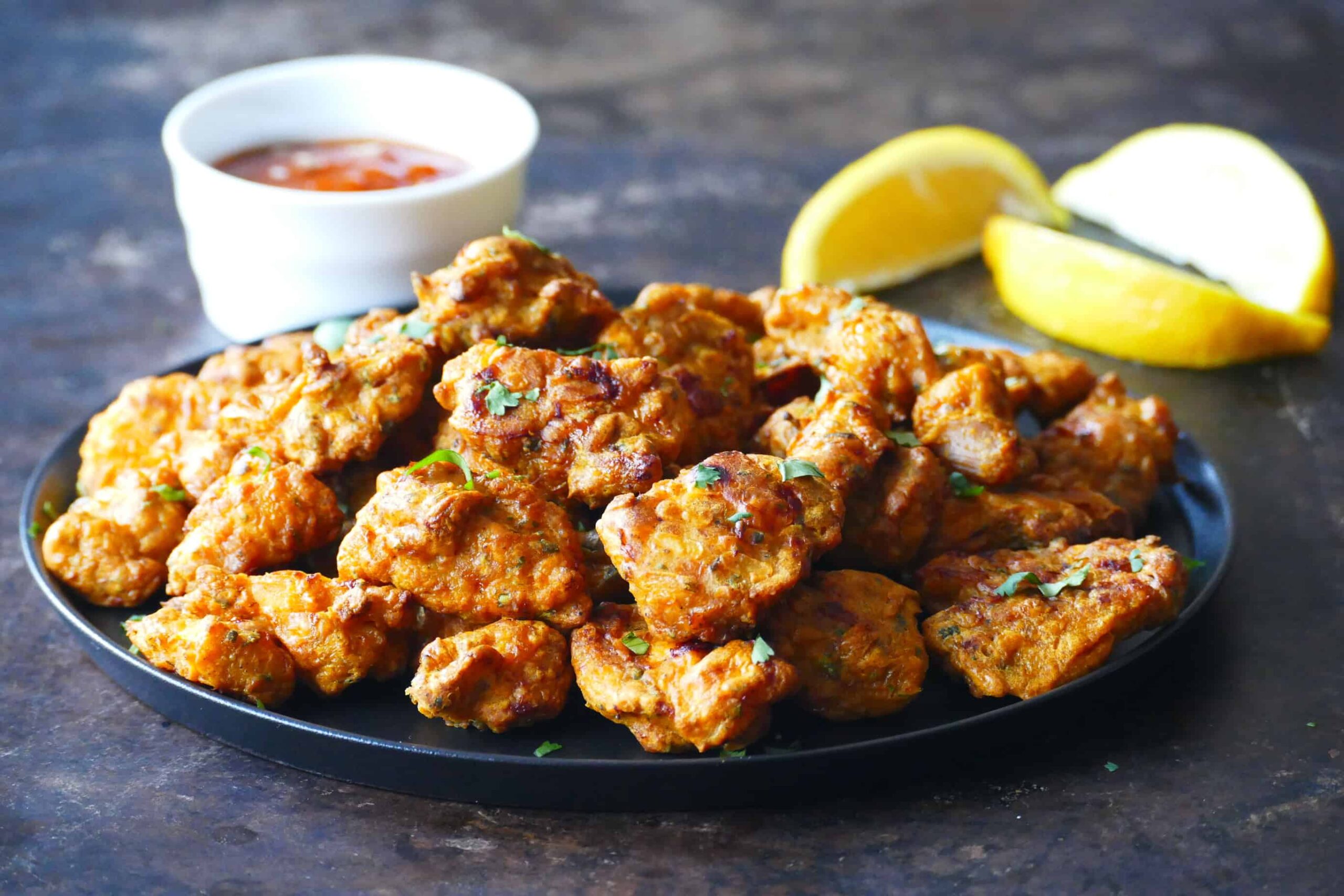 Golden colored chicken pieces garnished with cilantro. Lemon slices and sauce in background.