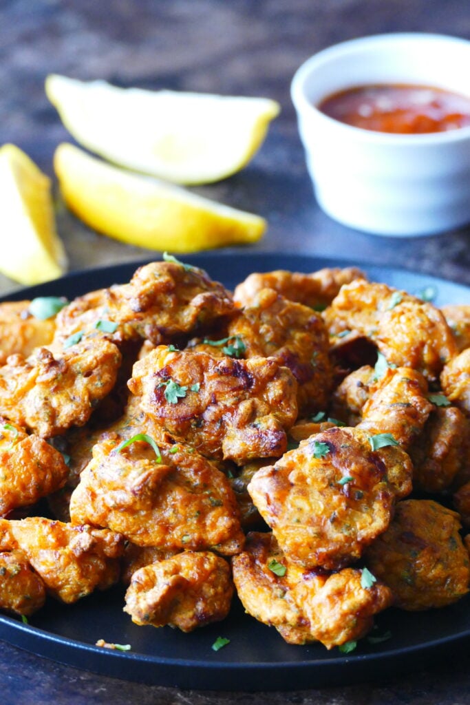 Golden colored chicken pieces garnished with cilantro. Lemon slices and sauce in background.