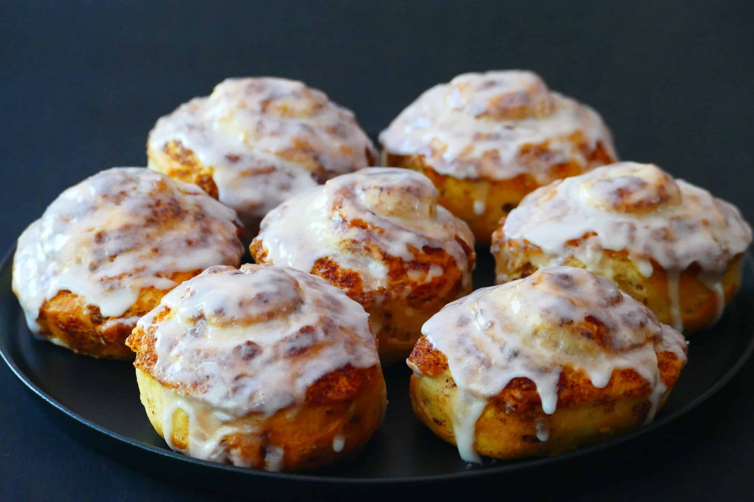 7 cinnamon rolls with icing on a black plate