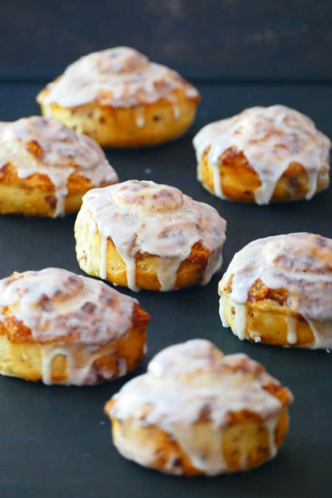 7 cinnamon rolls with icing on a black plate