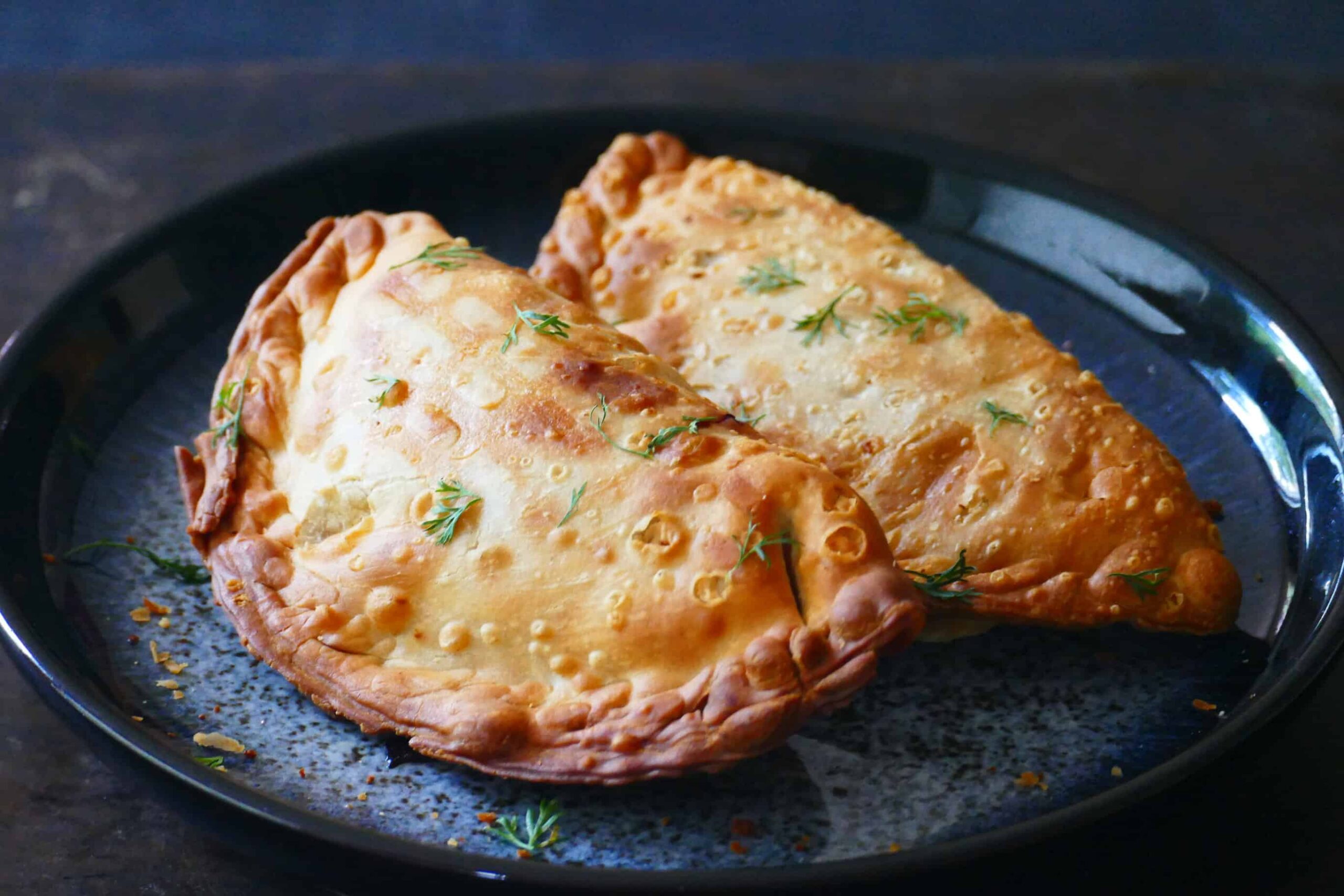 Two golden brown empanadas on blue plate