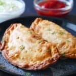 Two golden brown empanadas with white and red sauce