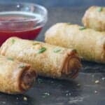 4 whole egg rolls and glass bowl with red chili sauce.