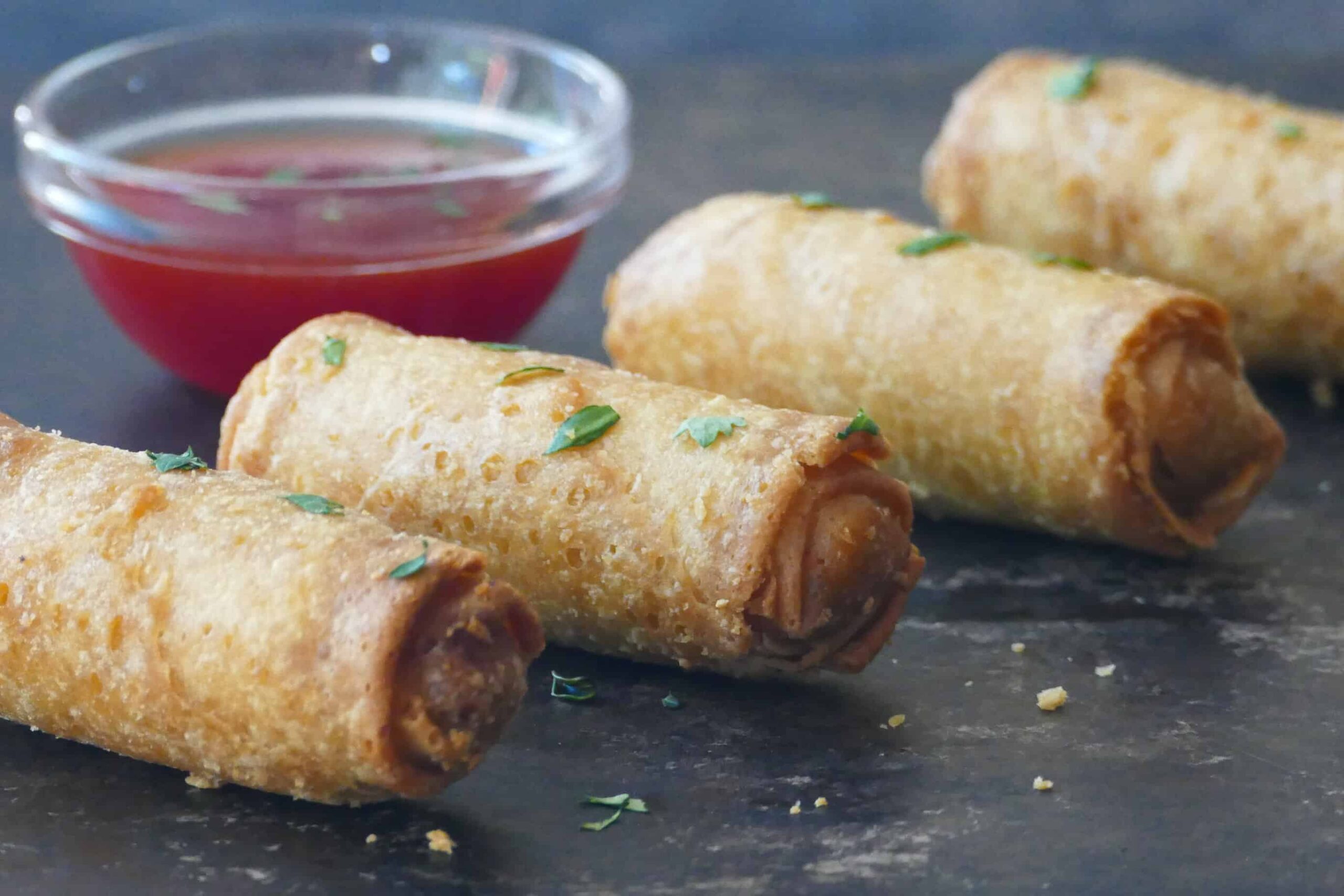 4 whole egg rolls and glass bowl with red chili sauce.