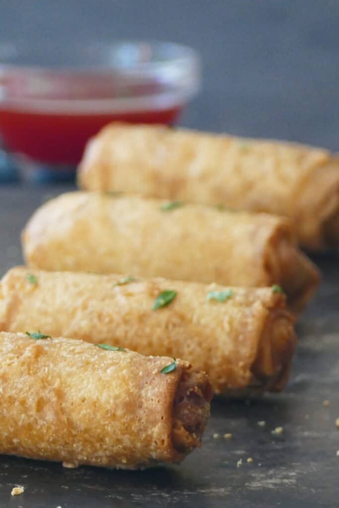 4 whole egg rolls and glass bowl with red chili sauce.