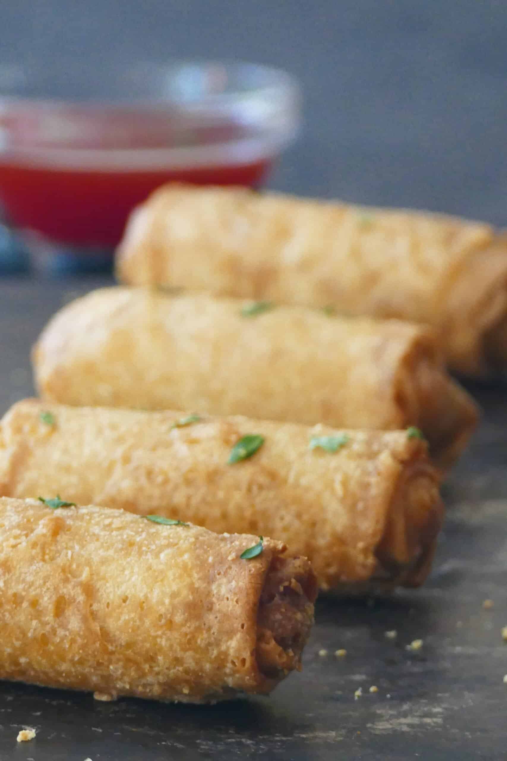 Air fryer frozen egg rolls - 4 whole egg rolls and glass bowl with red chili sauce.