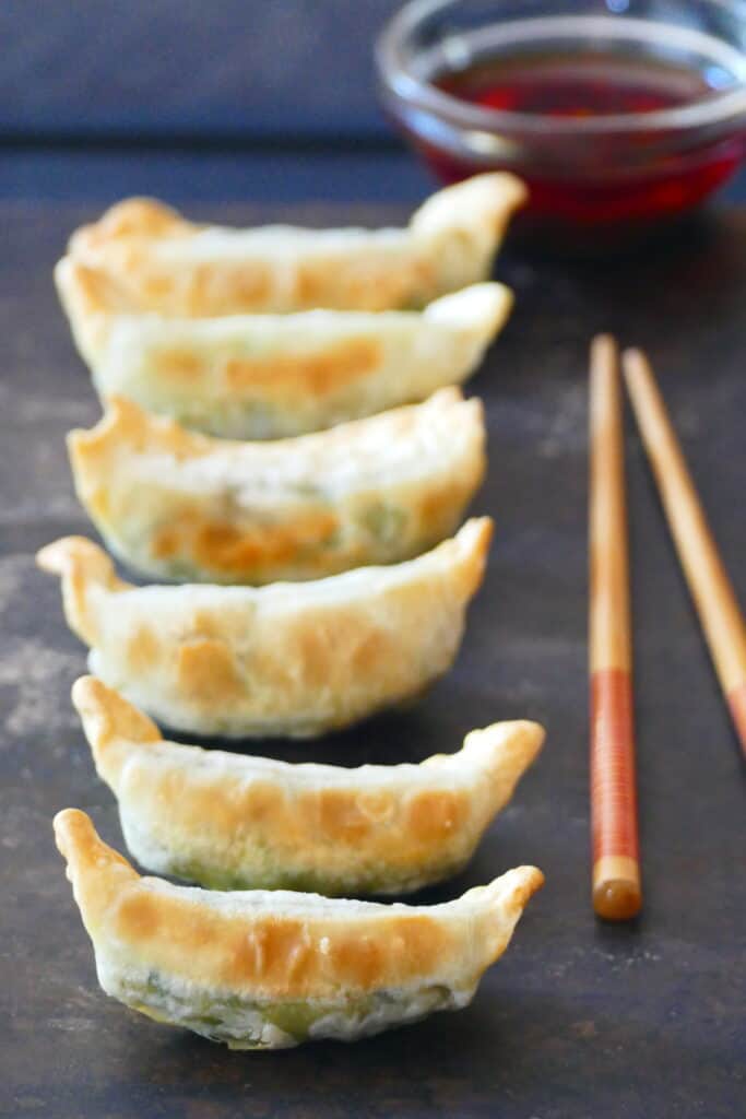 Golden gyoza potstickers in a row with chili sauce and chopsticks