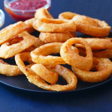 Onion rings on a black plate with red and white sauces in background