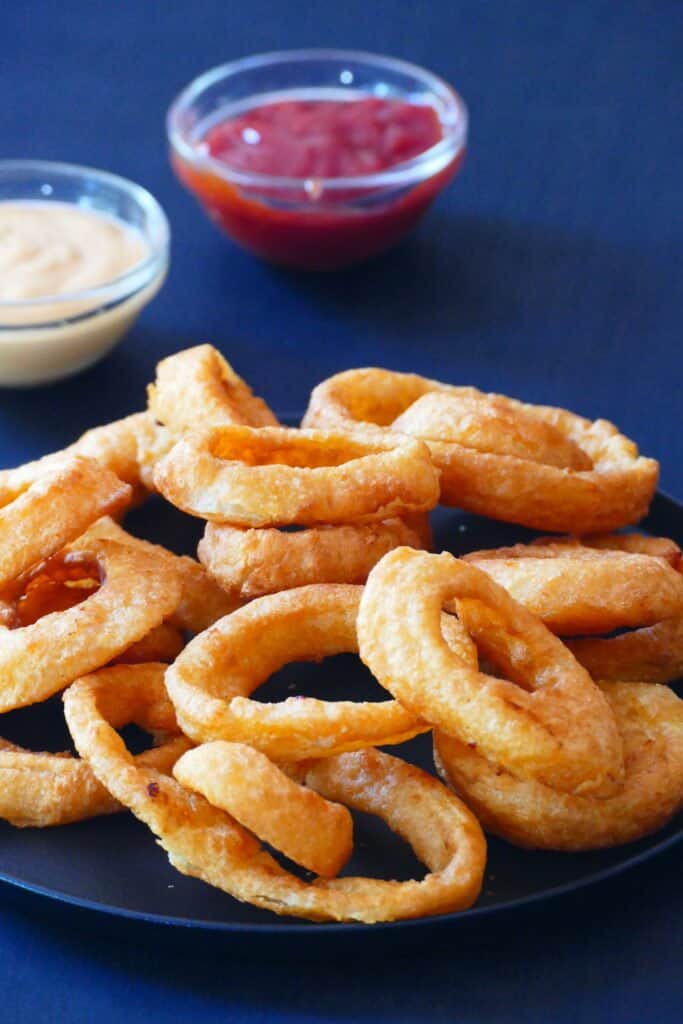 Onion rings on a black plate with red and white sauces in background