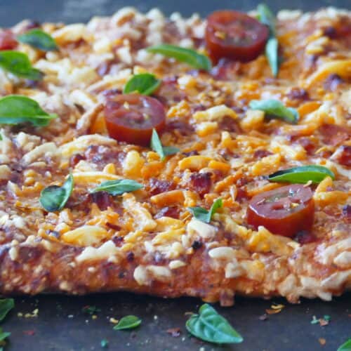 Pizza on dark surface with melted cheese and fresh tomato slices and basil