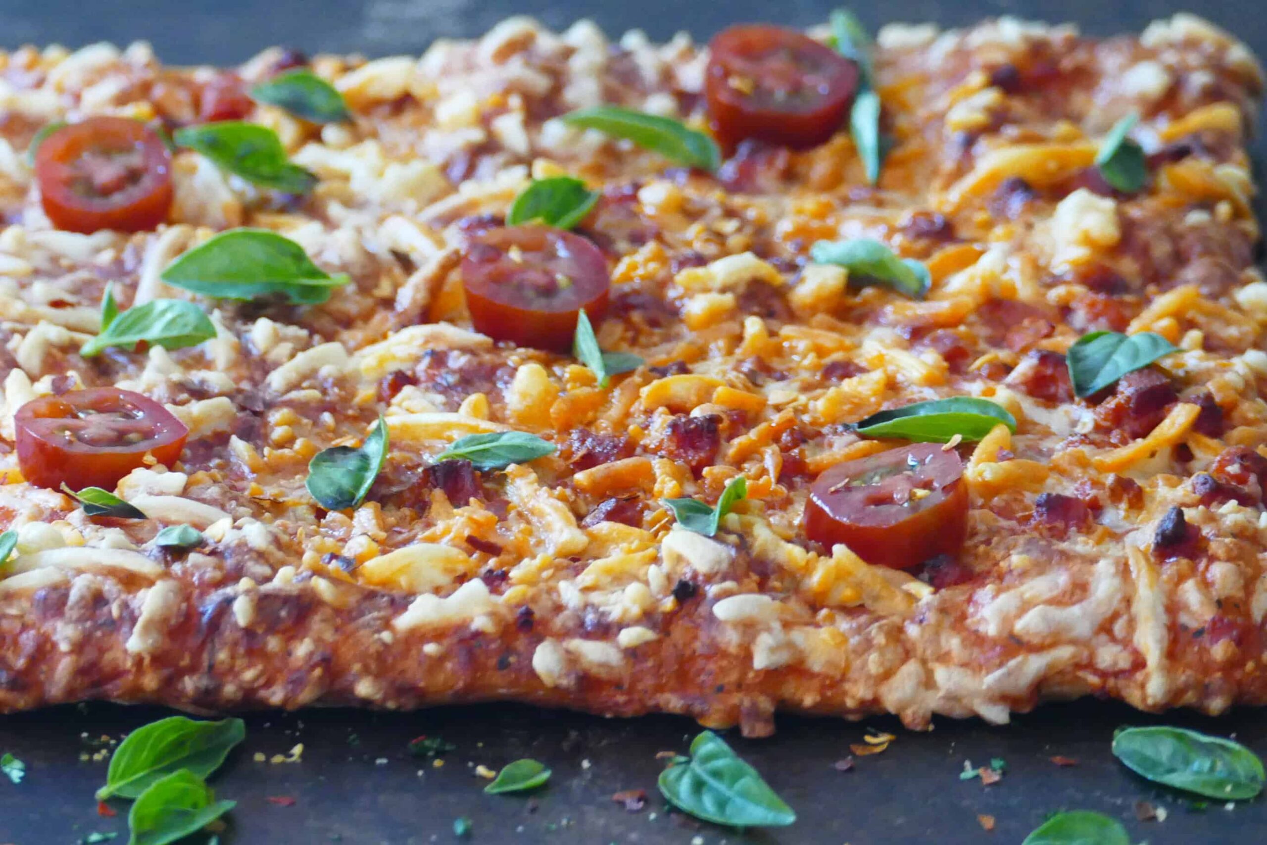 Pizza on dark surface with melted cheese and fresh tomato slices and basil