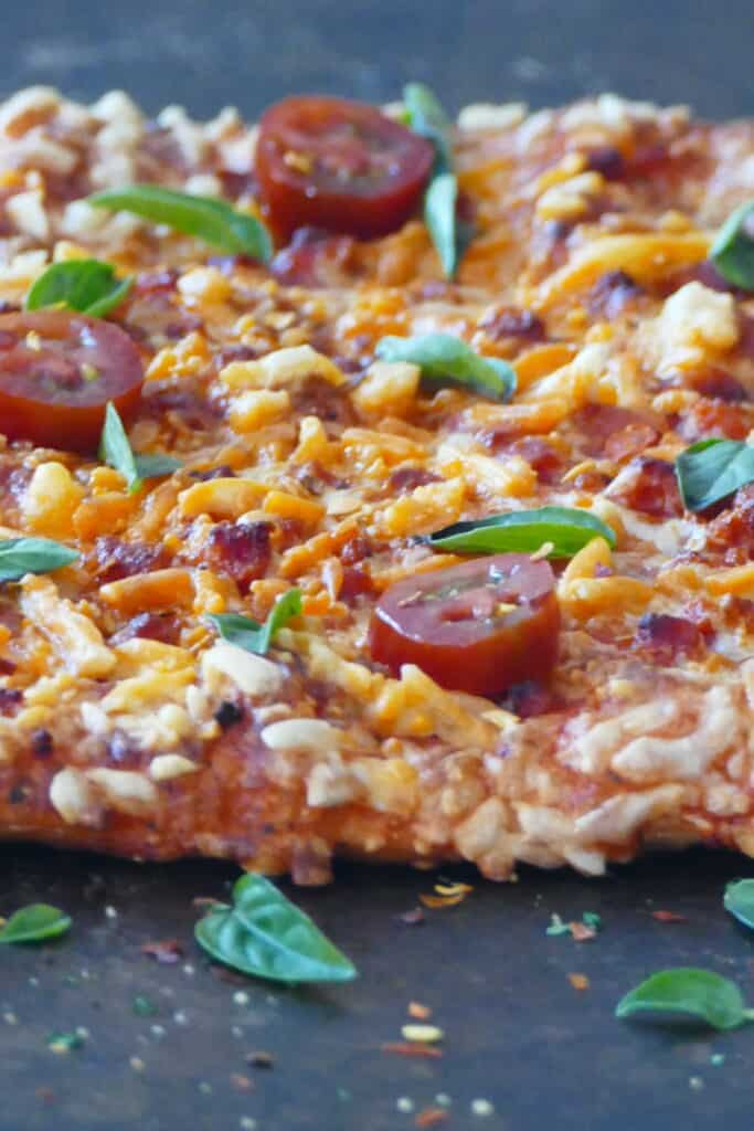 Pizza on dark surface with melted cheese and fresh tomato slices and basil