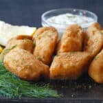 Golden fish fillets on dark surface with white sauce, dill and lemon