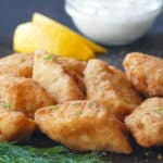 Golden fish fillets on dark surface with white sauce, dill and lemon