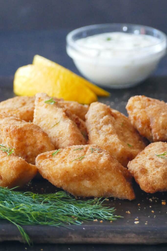 Golden fish fillets on dark surface with white sauce, dill and lemon