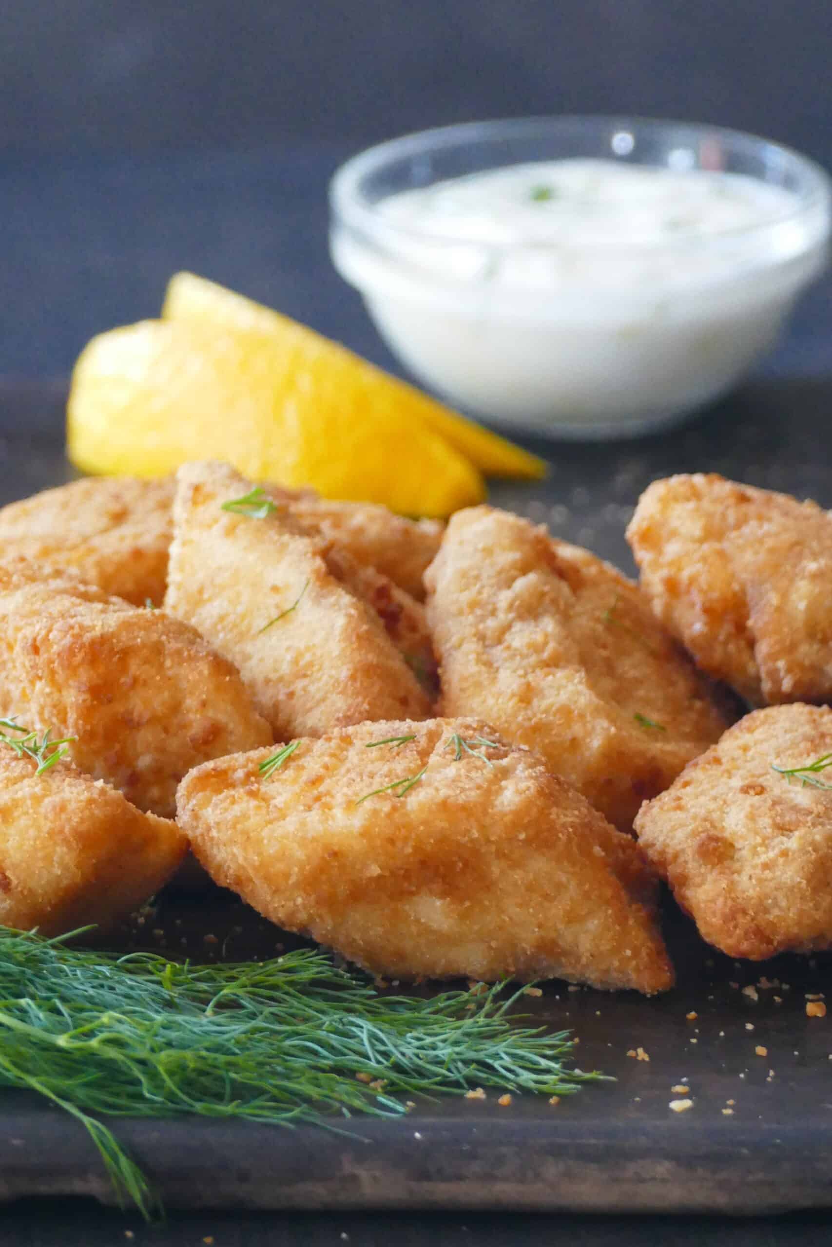 Frozen fish fillets in the air fryer - Golden fish fillets on dark surface with white sauce, dill and lemon