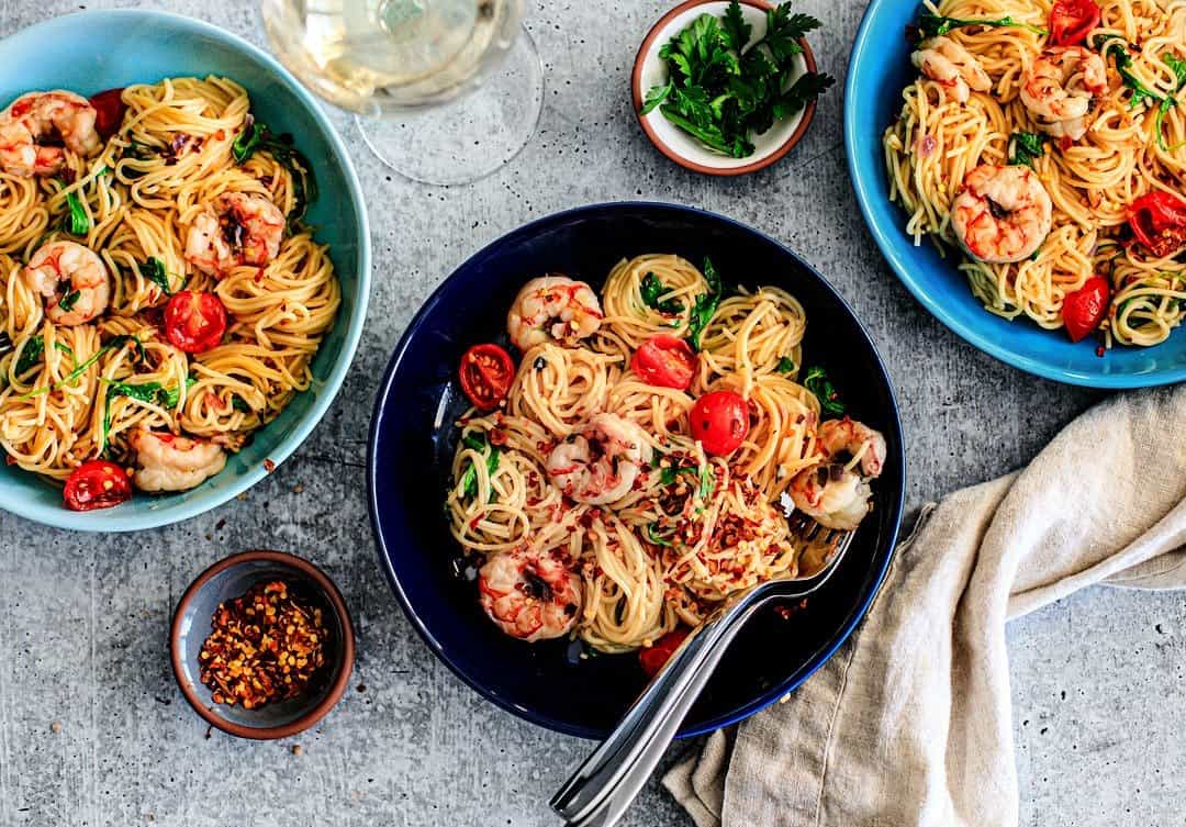 Three bowls of shrimp scampi with tomatoes, and red pepper flakes