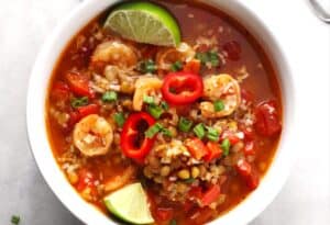 white bowl with red stew of lentils and shrimp, garnished with green onions and lime