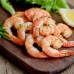 shrimp on dark cutting board with lemon wedge and rosemary, garnished with parsley