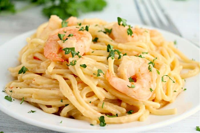 white plate with pasta and creamy sauce and shrimp on top, garnished with parsley