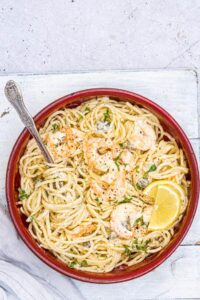 spaghetti with shrimp and creamy sauce garnished with lemons in a red bowl