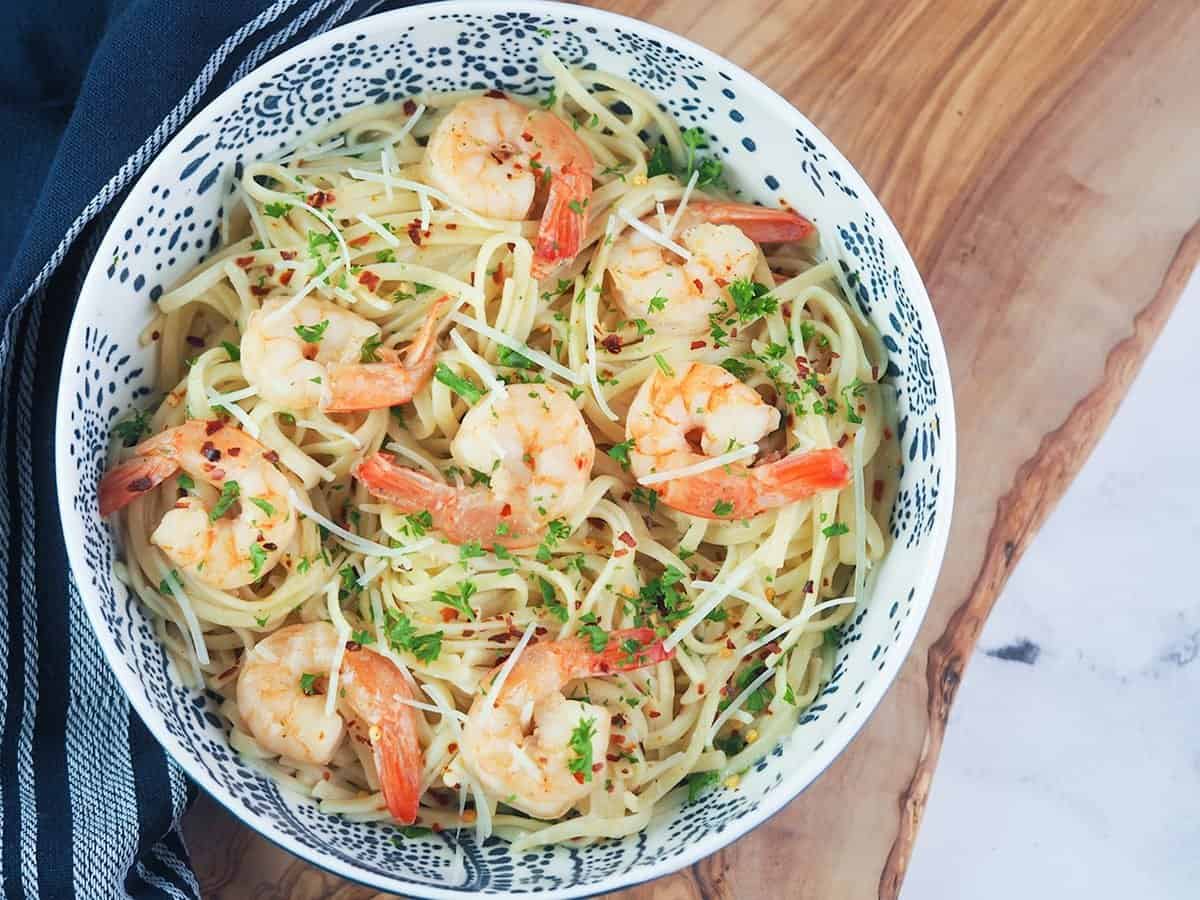 shrimp scampi pastain a blue and white bowl with parmesan and red pepper flakes on top