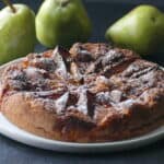 Air fryer pear tart with powdered sugar on white plate with three pears in background