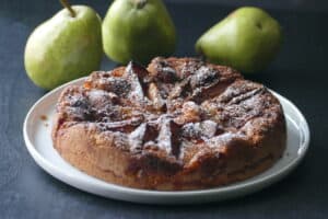 Air fryer pear tart with powdered sugar on white plate with three pears in background