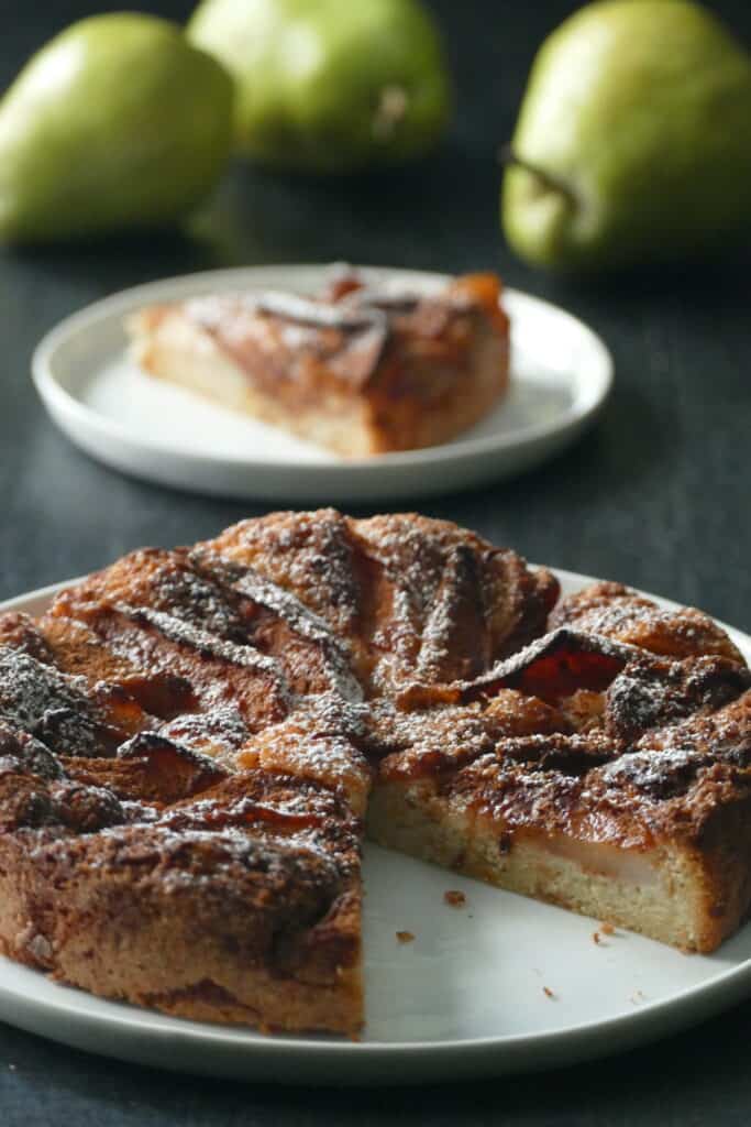 Air fryer pear tart with powdered sugar on white plate with three pears in background