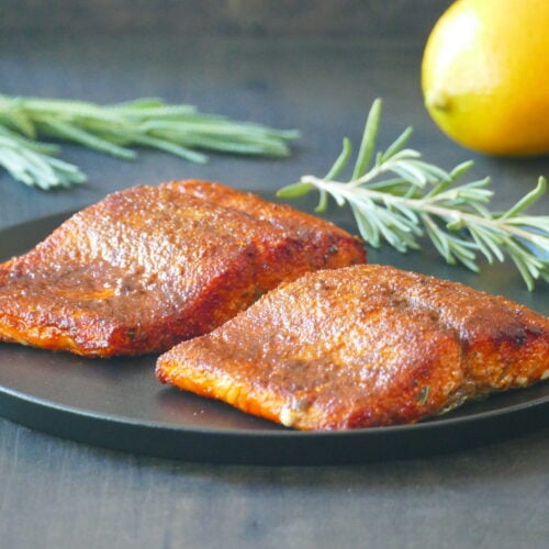 Two pieces of salmon with spices on a black plate