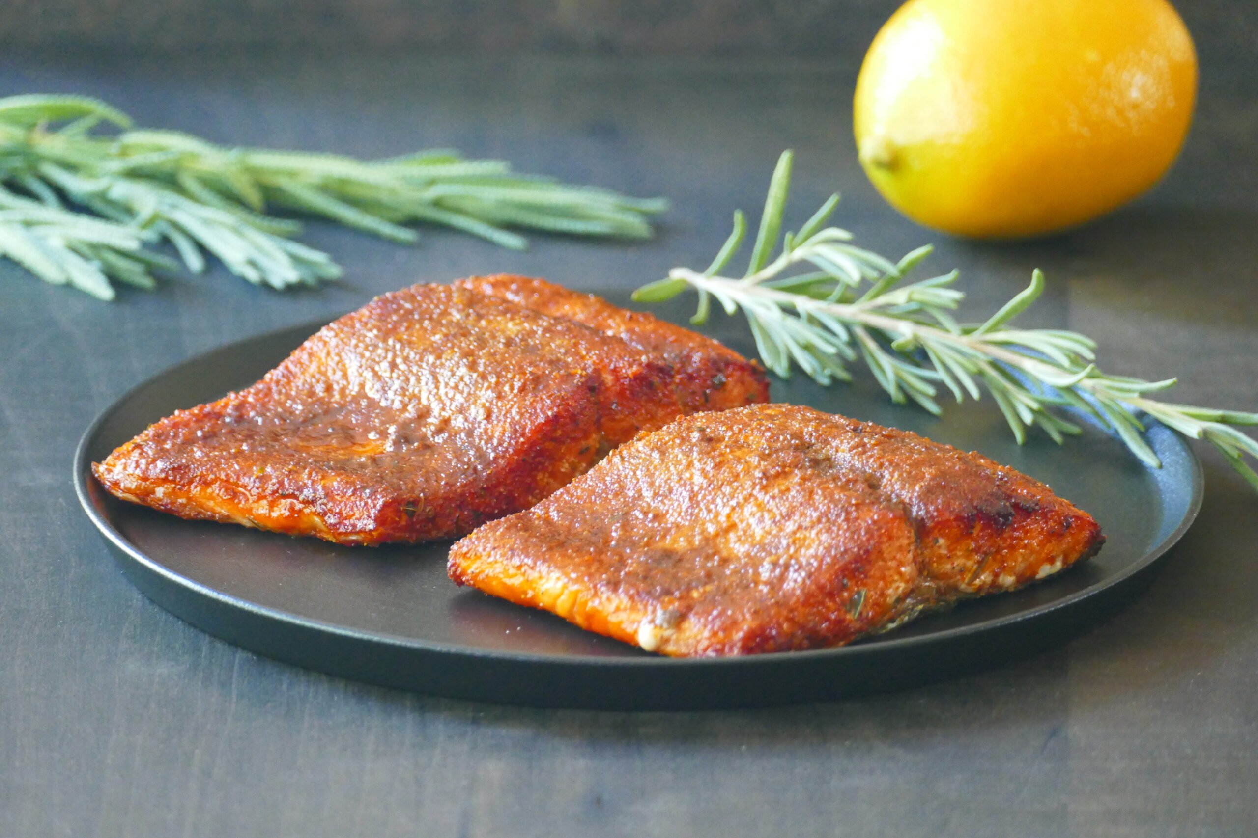 Two pieces of salmon with spices on a black plate