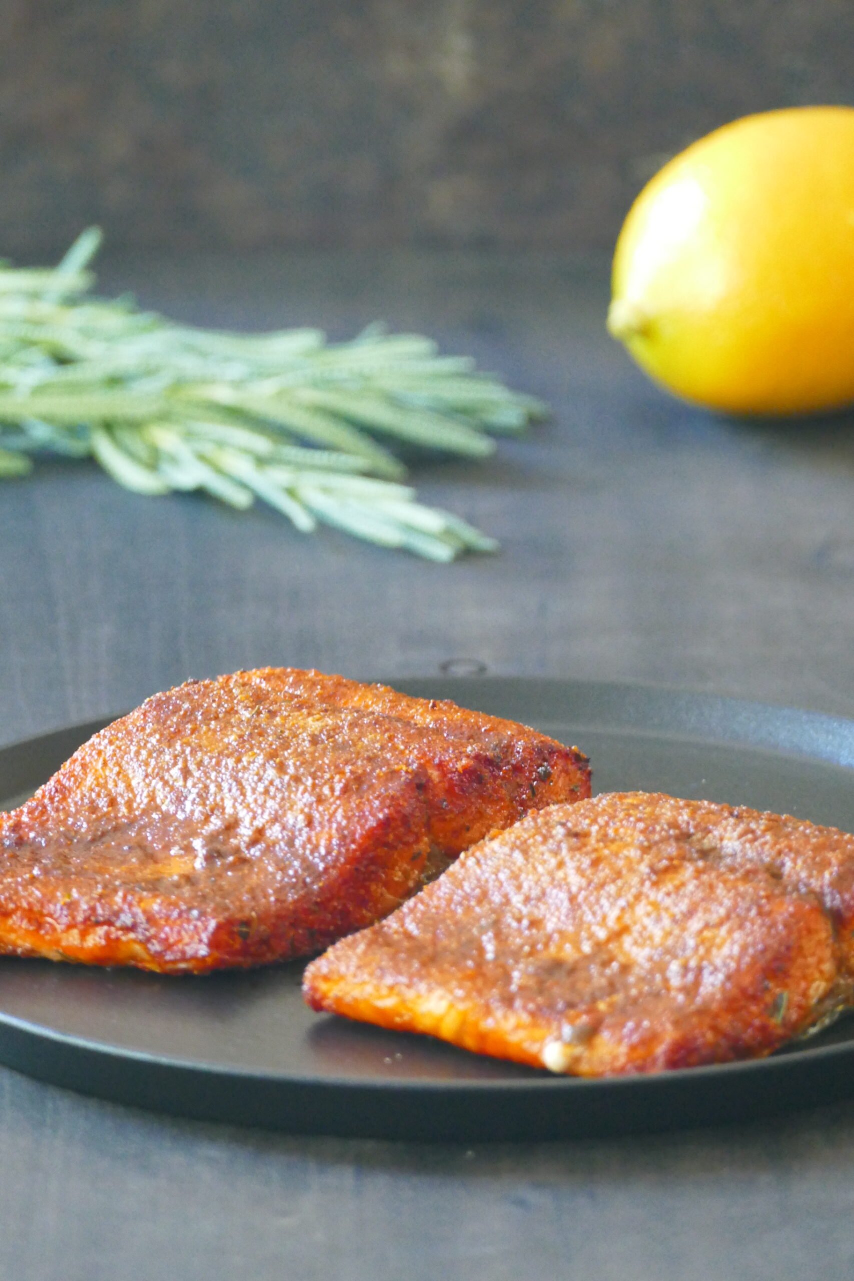 Instant Pot air fryer salmon: Two pieces of salmon with spices on a black plate