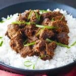 Beef rendang on a bed of rice in a black bowl