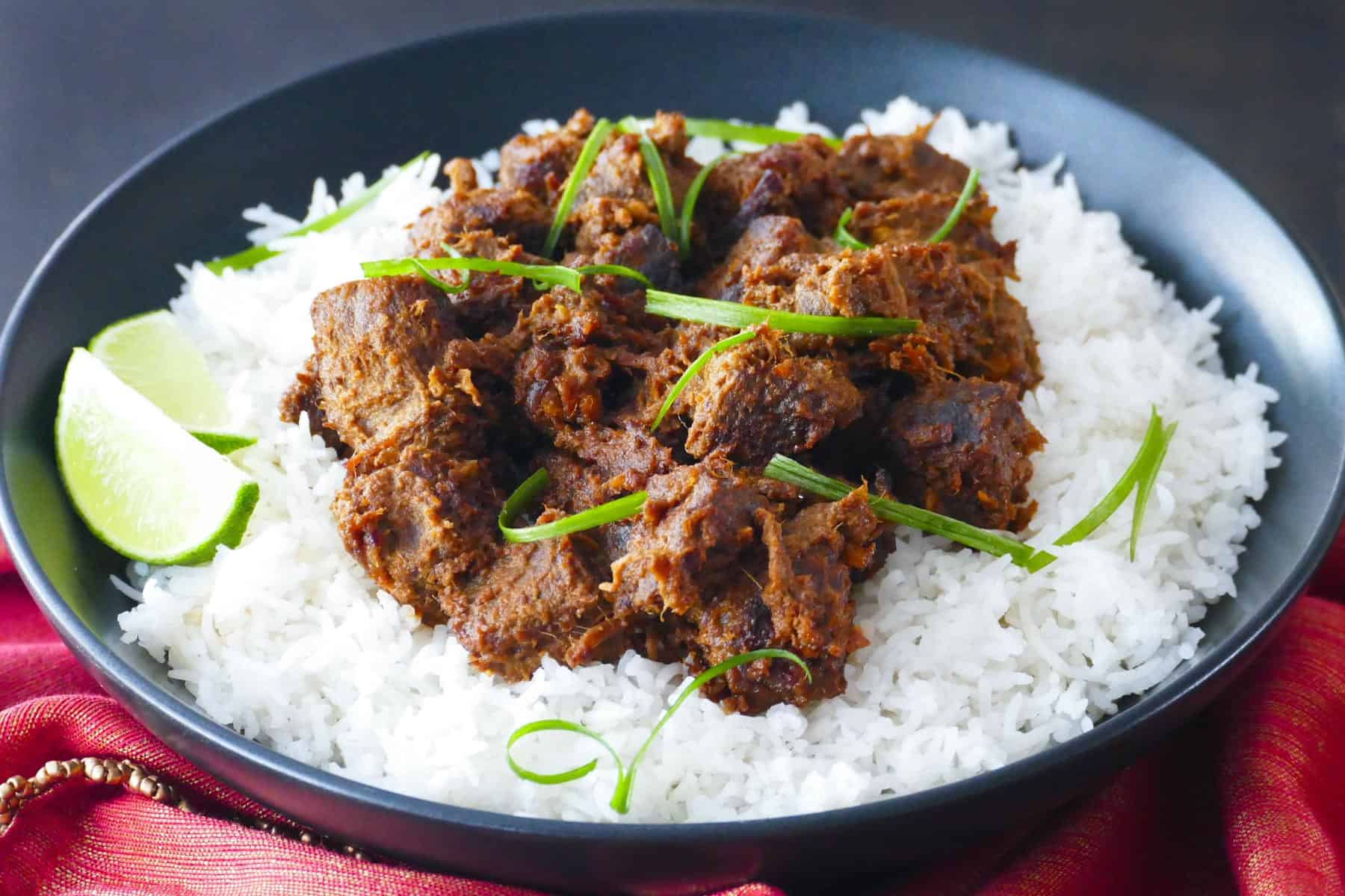 Beef rendang on a bed of rice in a black bowl