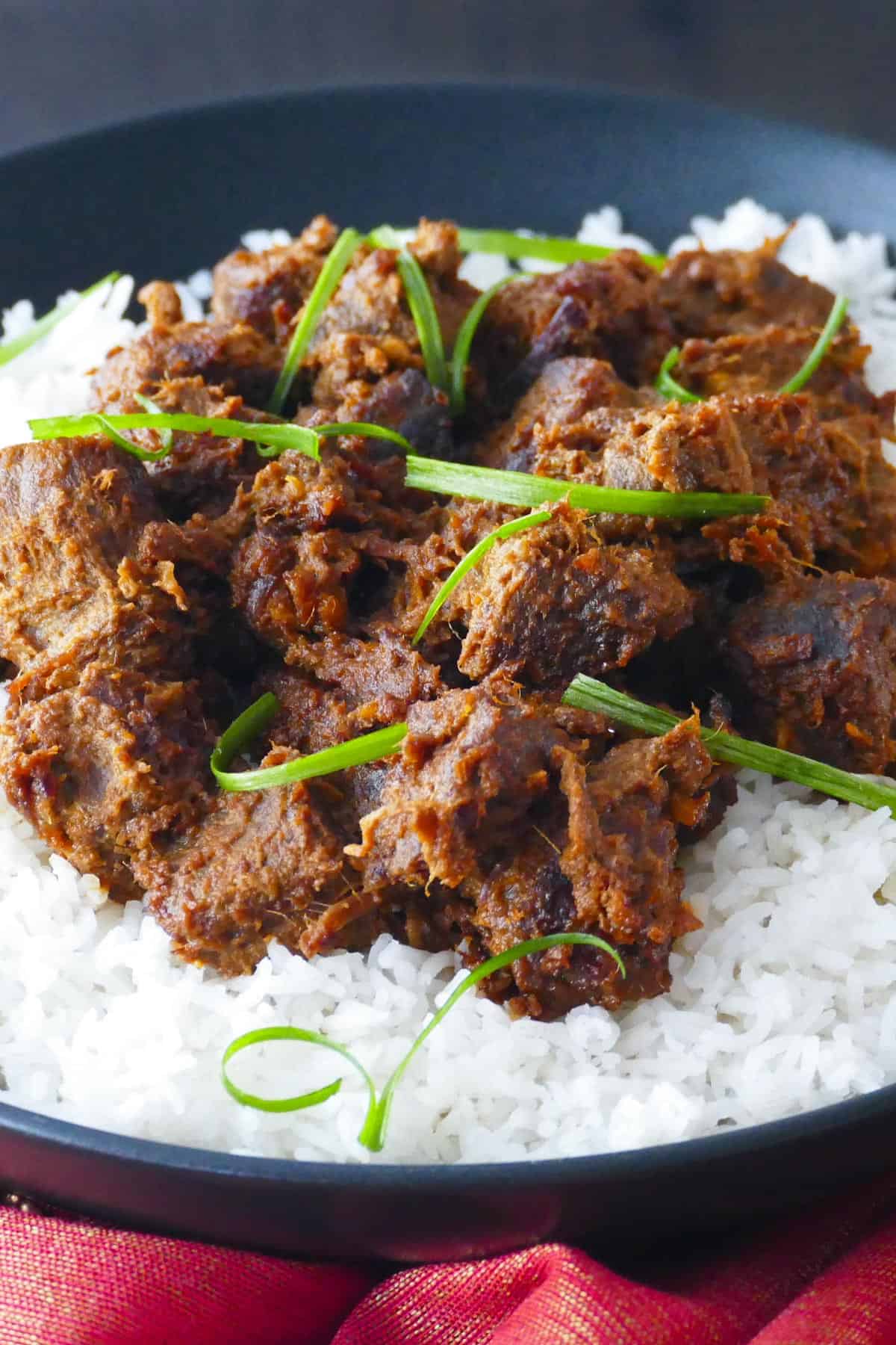 Beef rendang on a bed of rice in a black bowl