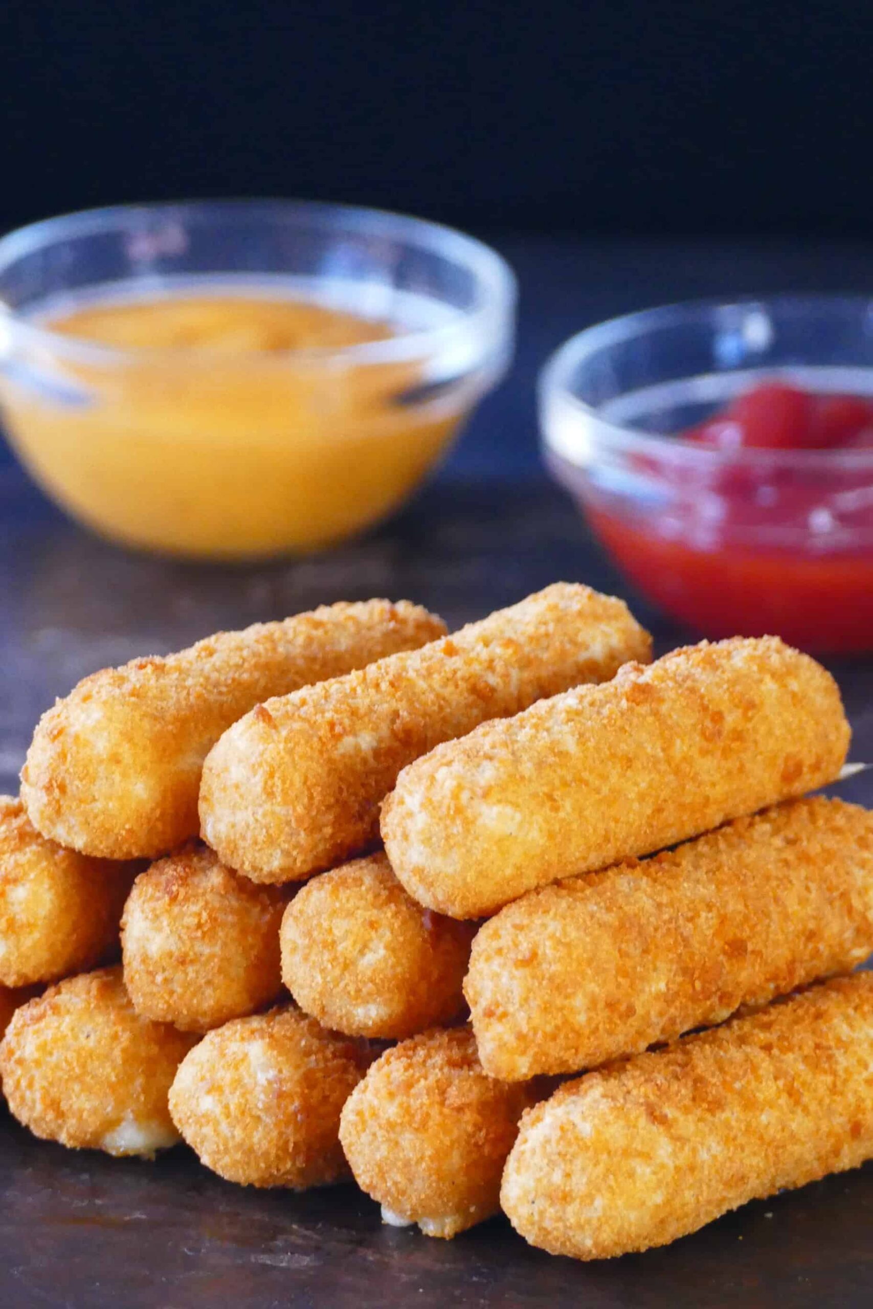 Air fryer frozen mozzarella sticks stacked on each other on dark surface