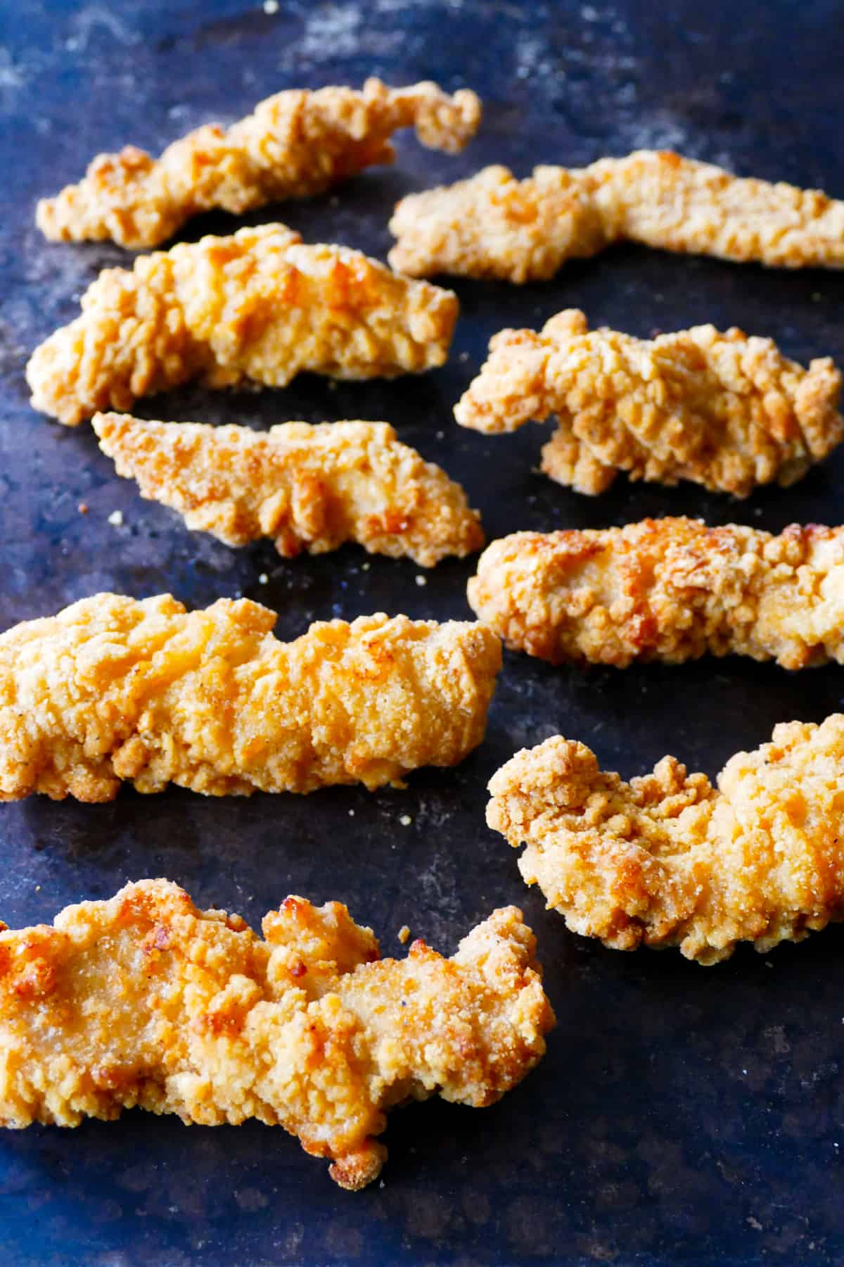 Air fryer frozen chicken tenders arranged in a row on dark background