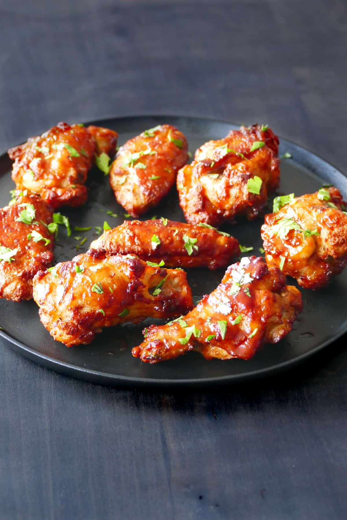 Air fryer frozen chicken wings  -Cooked chicken wings on black plate garnished with parsley