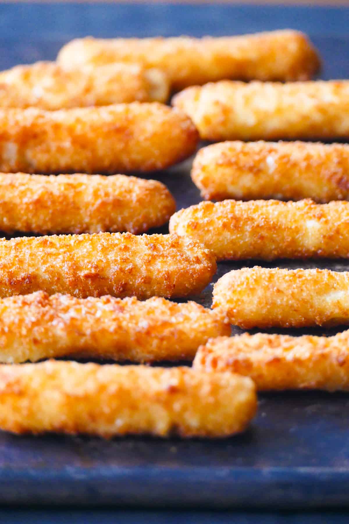 Air fryer frozen fish sticks laid out in a row on dark surface