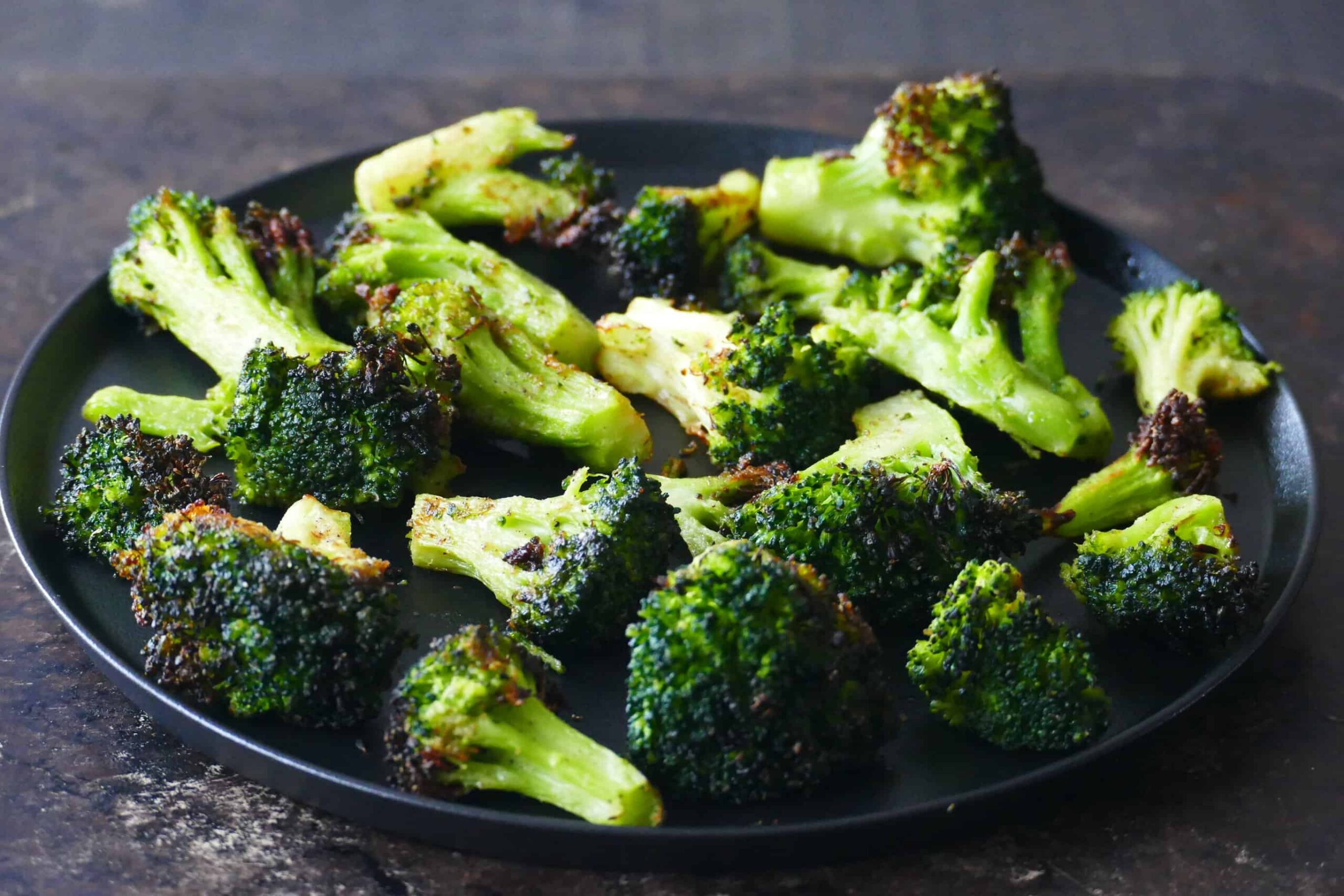 Black plate with slightly charred broccoli florets.