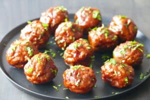 Glazed meatballs on a black plate, garnished with parsley
