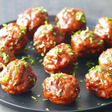 Glazed meatballs on a black plate, garnished with parsley