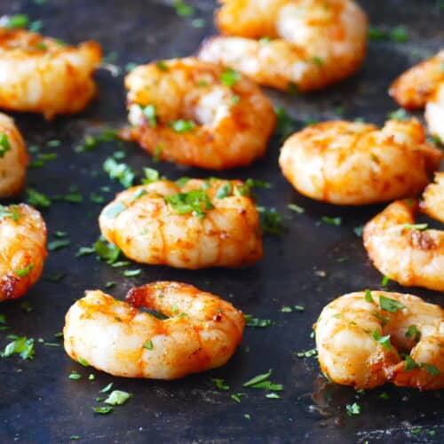 Cooked spiced shrimp arranged on a dark background with parsley garnish.