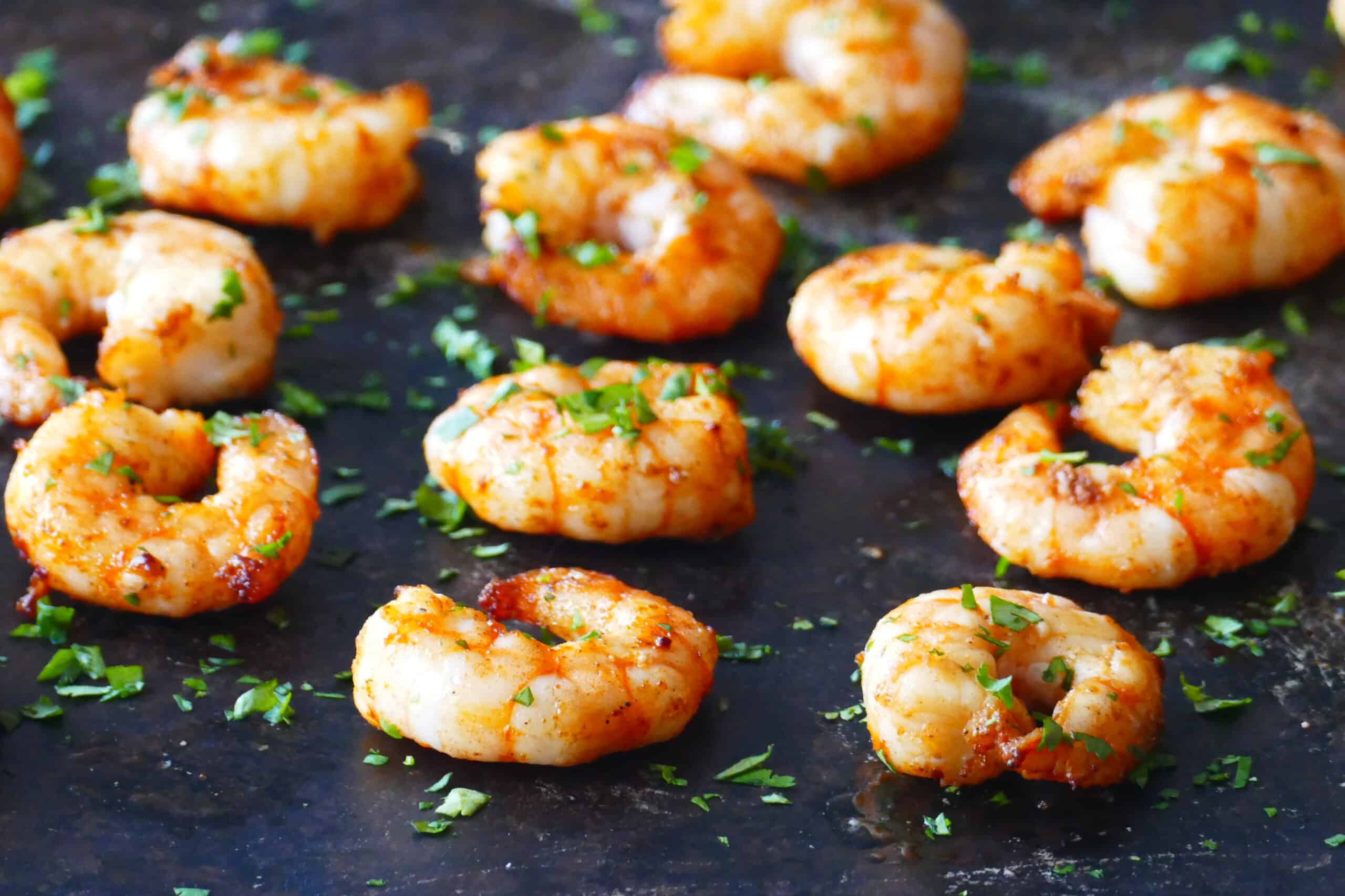 Cooked spiced shrimp arranged on a dark background with parsley garnish.