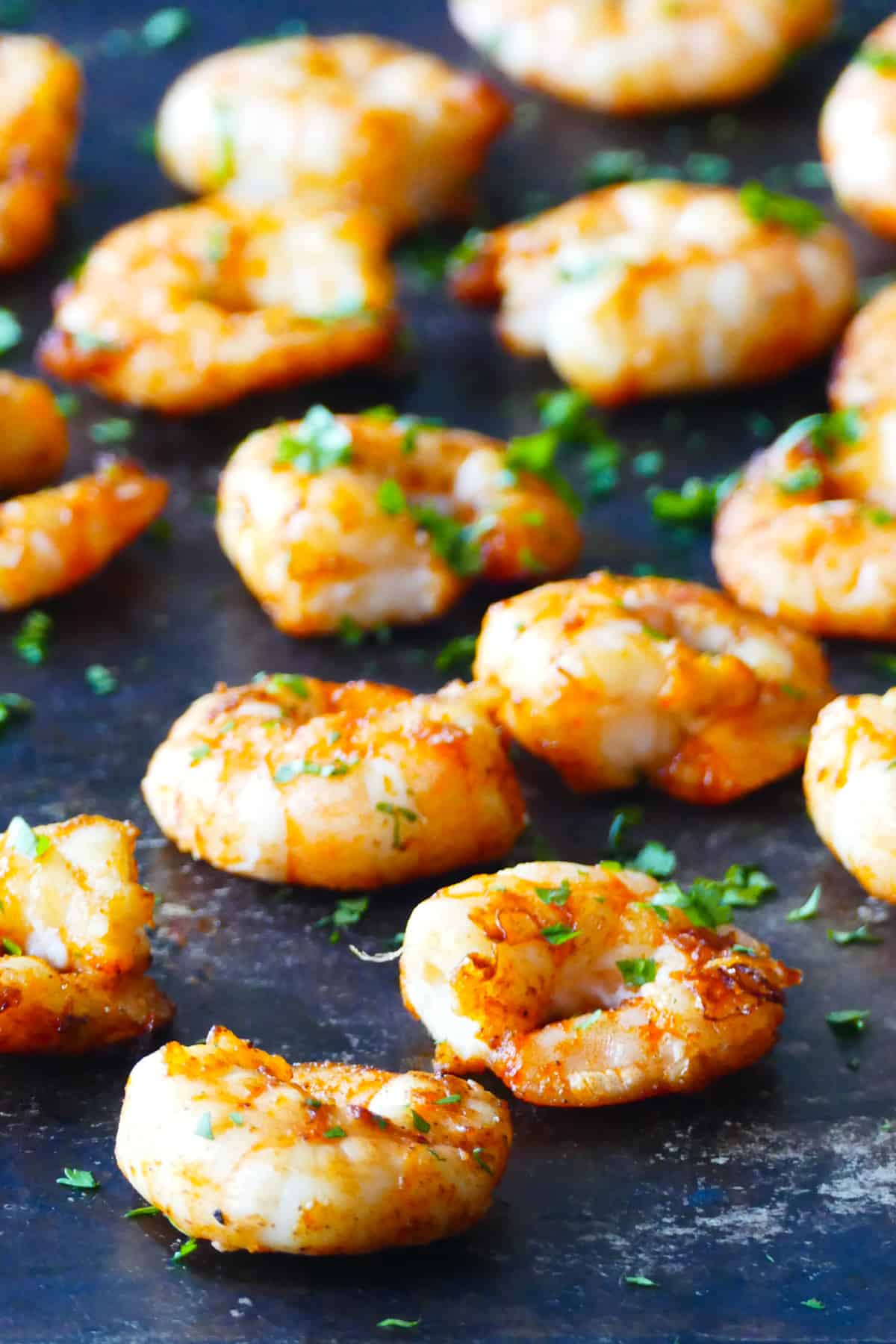 Air fryer frozen shrimp - Cooked spiced shrimp arranged on a dark background with parsley garnish.