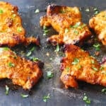 Tandoori chicken with charred bits on dark surface with cilantro garnish