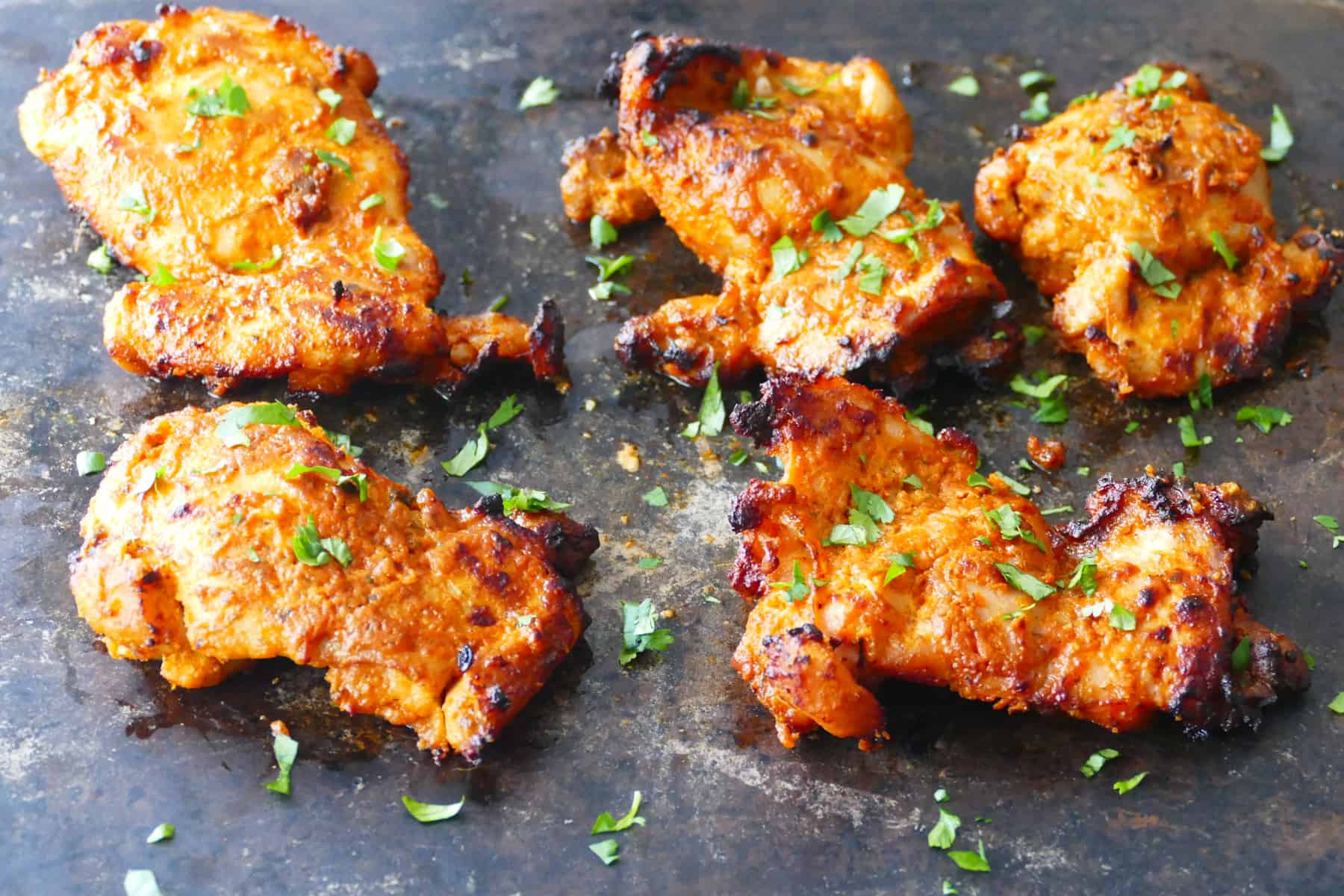 Tandoori chicken with charred bits on dark surface with cilantro garnish