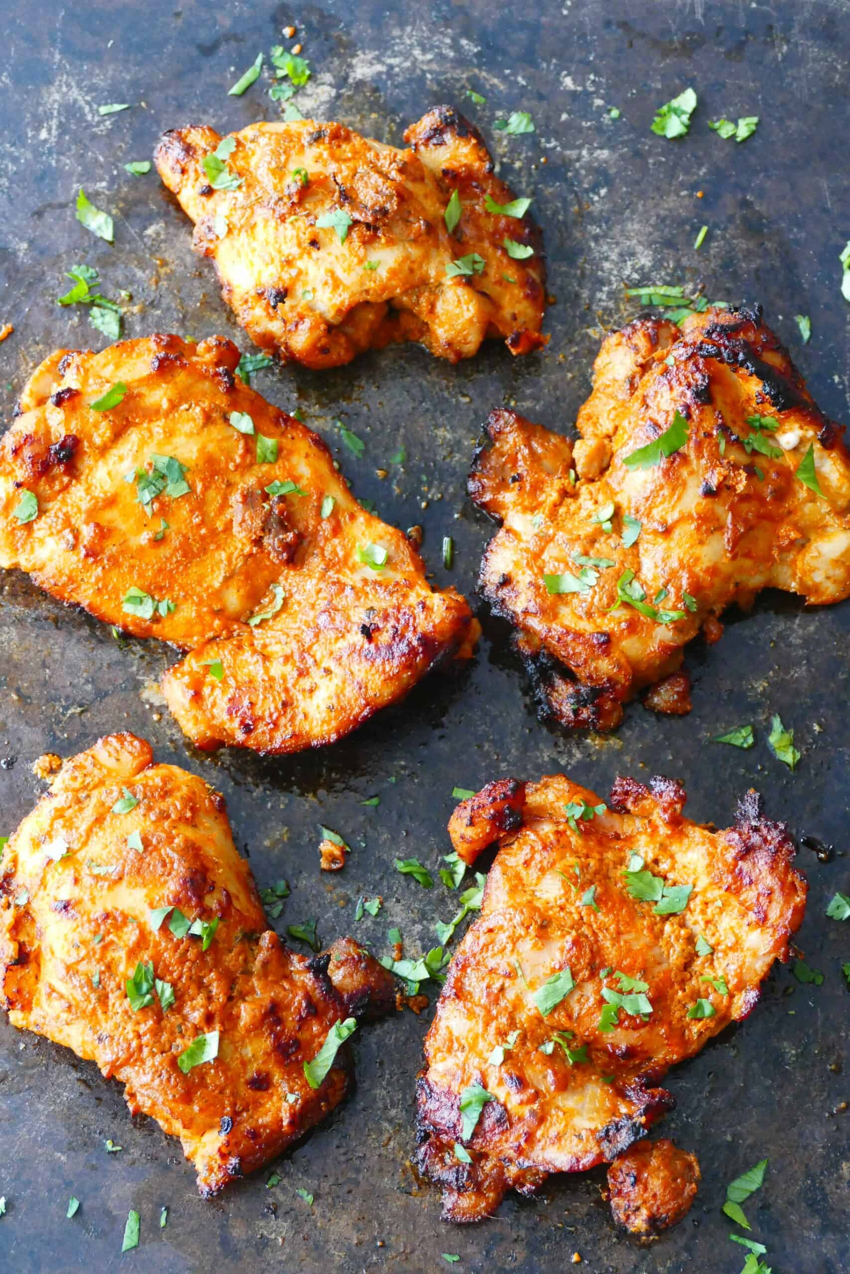 Air fryer tandoori chicken with charred bits on dark surface with cilantro garnish