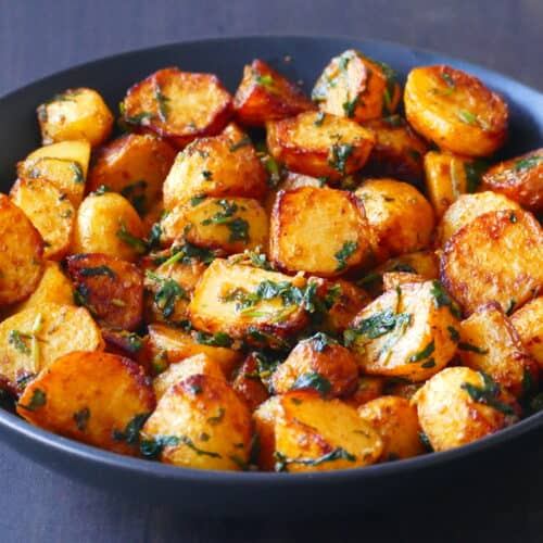 Black bowl with golden roasted potatoes coated with cilantro sauce